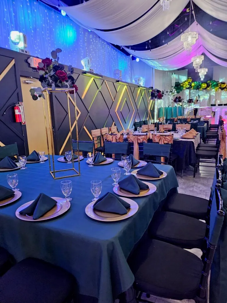 A table set in teal linen with charger plates and a floral centrepiece.